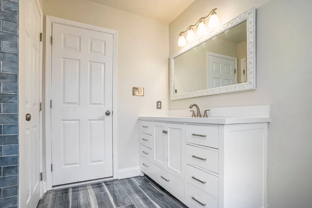 Modern bathroom remodel with white vanity cabinets, quartz countertop, and decorative mirror frame by Pottstown Construction