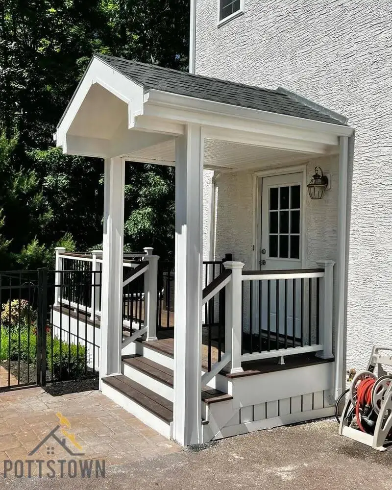 White covered porch addition with black metal railing, composite deck, and black shingle roof on brick home