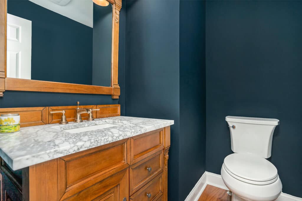 Modern bathroom remodel with marble countertop, wood vanity cabinet, and dark teal painted walls