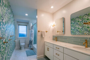 Modern bathroom remodel with green patterned wallpaper, white vanity, marble countertops, and brass fixtures