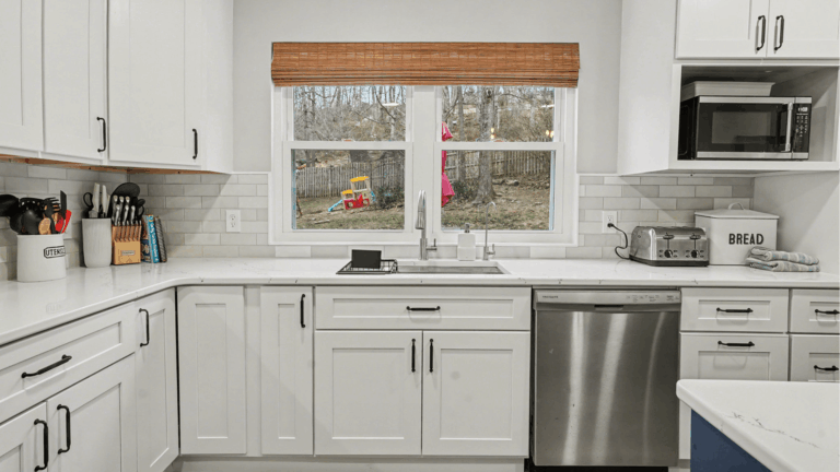 Modern white shaker kitchen with quartz countertops, stainless steel appliances, and natural wood window valance