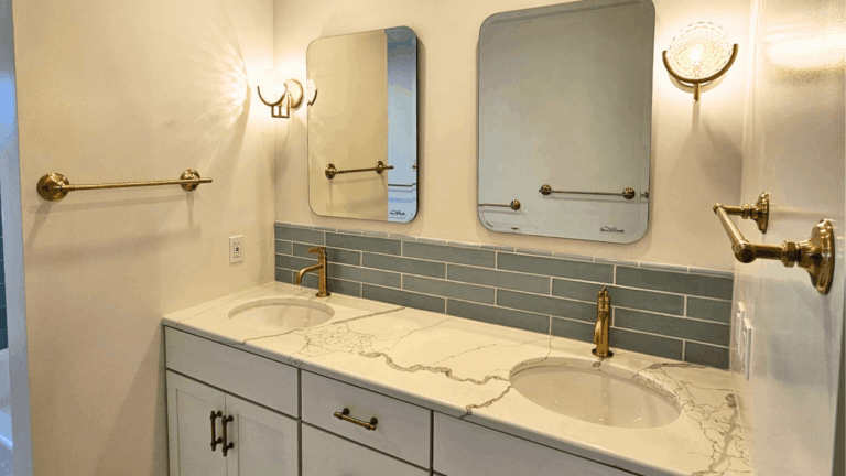 Modern bathroom remodel with dual vanity, marble countertop, gray tile backsplash, and brass fixtures