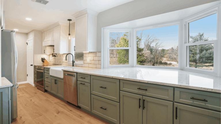 Modern kitchen remodel with green shaker cabinets, quartz countertops, subway tile backsplash, and large windows overlooking wooded landscape