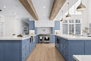 Modern kitchen remodel with blue shaker cabinets, white quartz countertops, exposed wood beams, and stainless steel appliances
