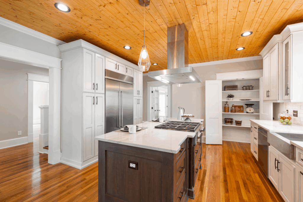 Modern kitchen remodel with white shaker cabinets, wood ceiling, island with gas cooktop, stainless steel appliances, and hardwood flooring.