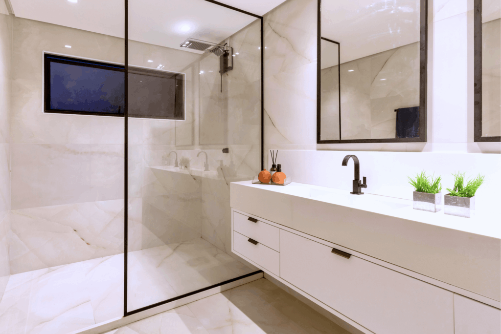 Modern luxury bathroom remodel with marble tile, glass shower enclosure, and white vanity with dark fixtures