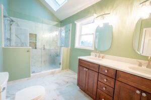 Modern master bathroom remodel with marble tile, glass shower enclosure, wood vanity, and green painted walls.