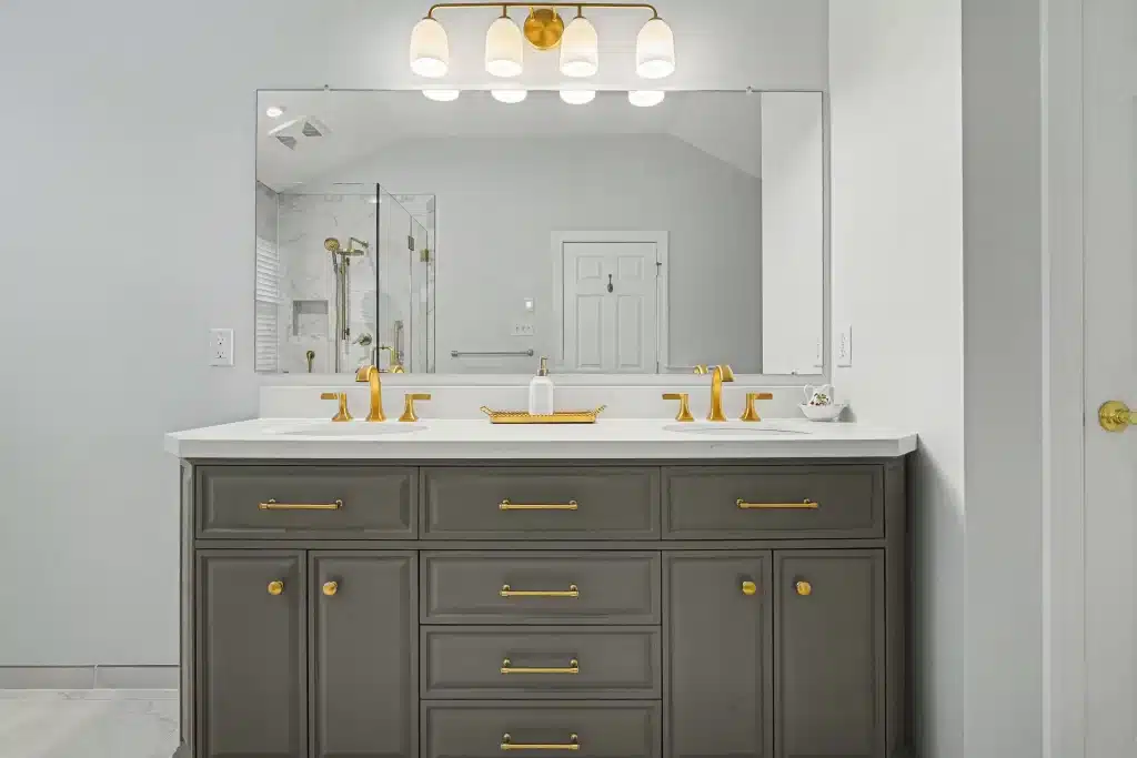 Modern master bathroom vanity with dual sinks, olive green cabinets, gold fixtures, and large mirror with LED lighting
