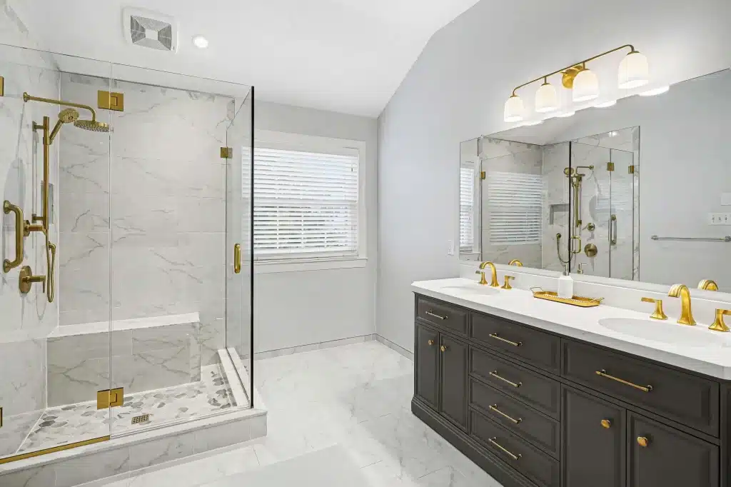 Luxury master bathroom remodel with marble tile, glass shower enclosure, dual vanity with dark cabinetry and brass fixtures