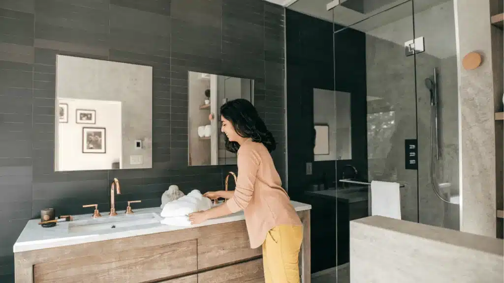 Modern bathroom remodel with dark tile, floating wood vanity, marble countertop, and frameless glass shower enclosure