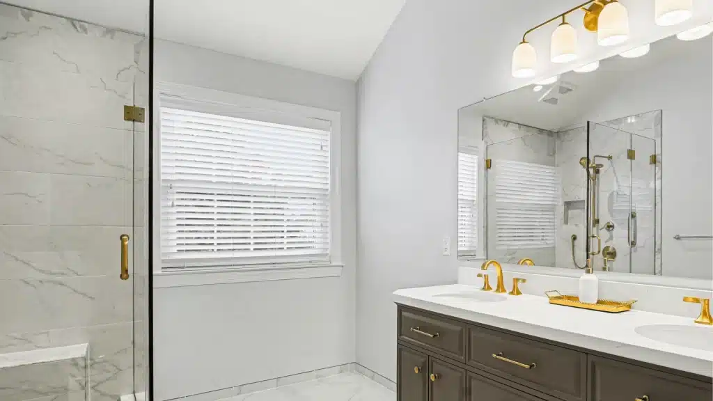 Modern luxury bathroom remodel with marble tile shower, glass enclosure, dark vanity, and brass fixtures