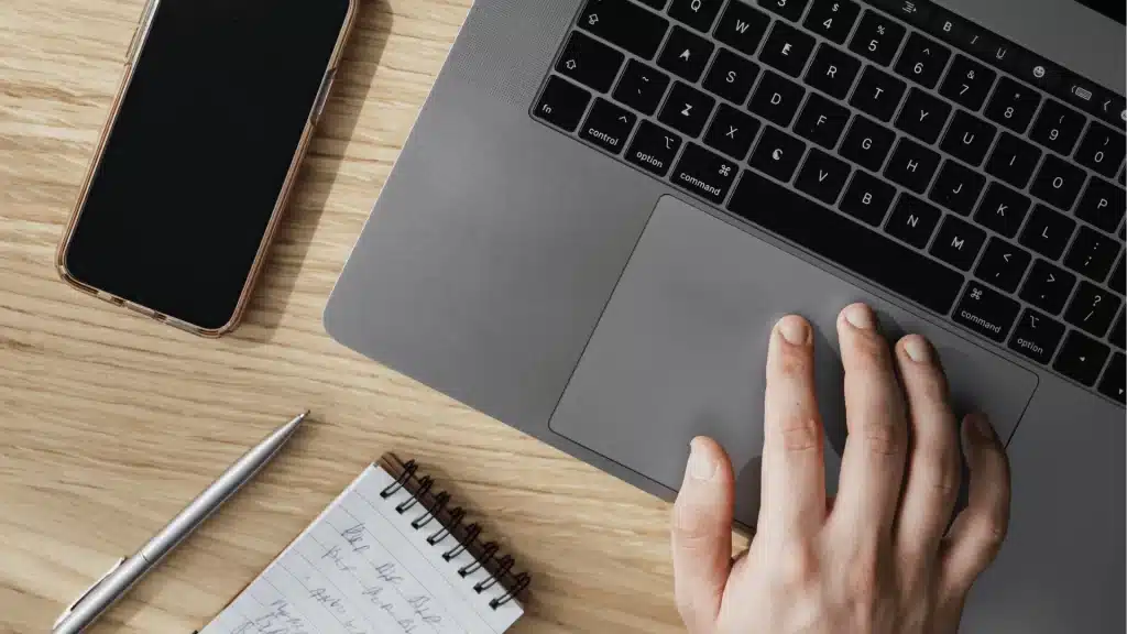 Laptop keyboard and touchpad with smartphone, notepad, and pen on wooden desk