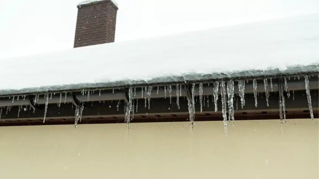 Frozen gutters and ice dams on residential roofline showing winter roof damage and poor drainage
