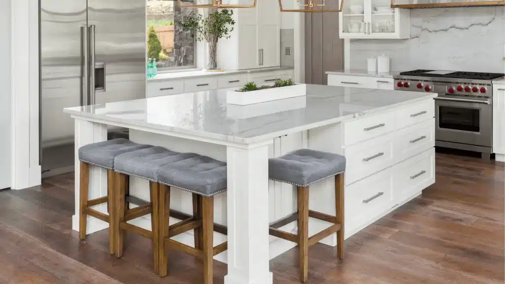 Modern white kitchen with quartz island, stainless steel appliances, and wood bar stools.
