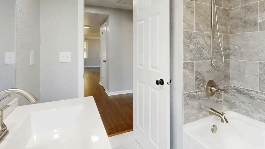 Modern master bathroom renovation with marble tile shower, white vanity, and wood flooring by Pottstown Construction Company