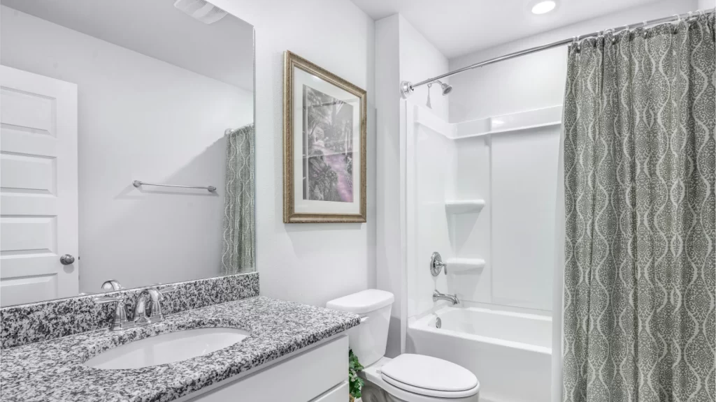 Modern bathroom remodel with granite countertops, framed mirror, and shower-tub combo with patterned curtain