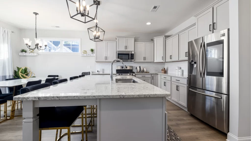 Bright kitchen remodel with light gray shaker cabinets, granite island countertop, stainless steel appliances, and black chandelier pendant lights