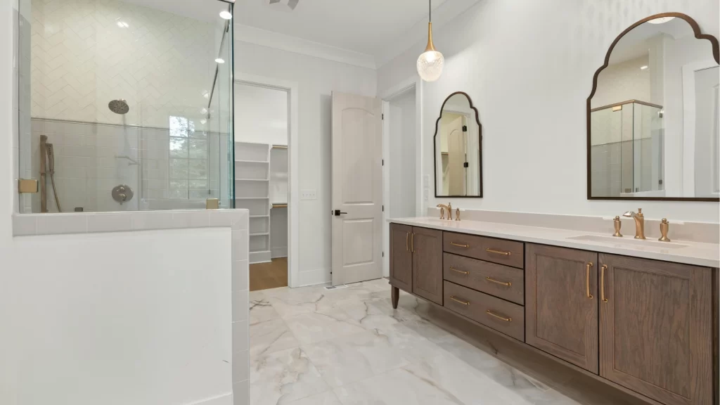 Modern master bathroom remodel with marble flooring, walk-in shower, dual vanity with dark wood cabinets, and brass fixtures.