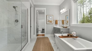 Modern primary bathroom remodel with marble tile shower, freestanding soaker tub, and gray vanity cabinets with white countertops.