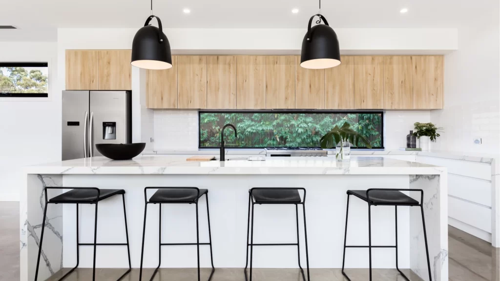 Modern kitchen material pairing with white lower cabinets, light wood upper cabinets, marble waterfall island, and black matte pendant lights and barstools