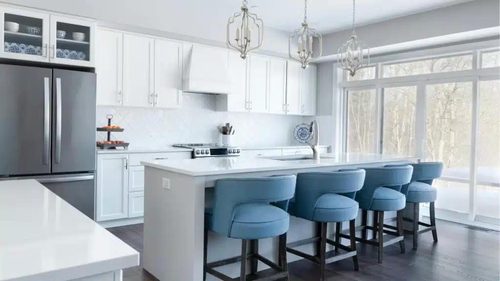 Modern white kitchen remodel with island, quartz countertops, stainless steel appliances, and blue bar stools