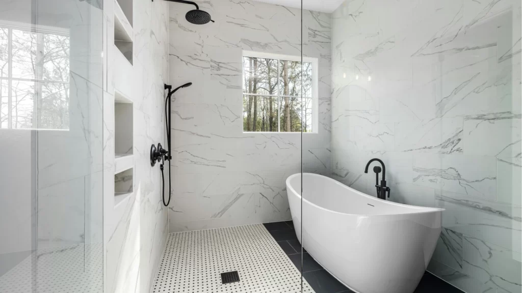 Modern luxury bathroom remodel with marble tile walls, freestanding white soaker tub, and walk-in shower with glass enclosure