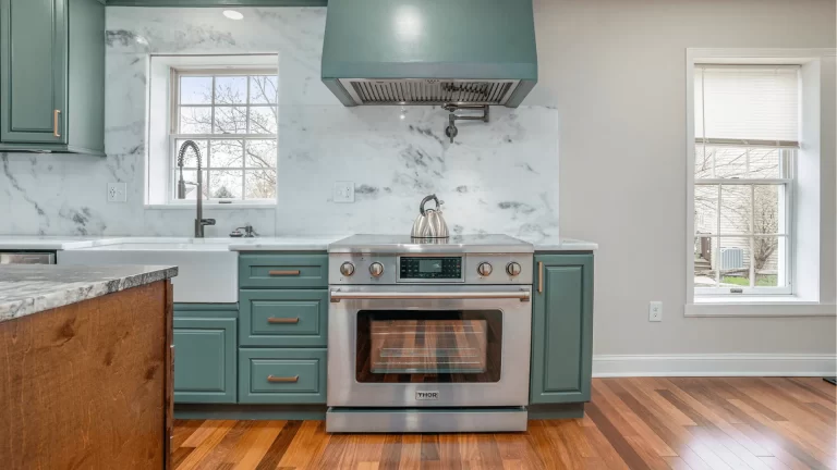 Modern kitchen remodel with teal cabinetry, marble countertops, stainless steel range, and hardwood floors