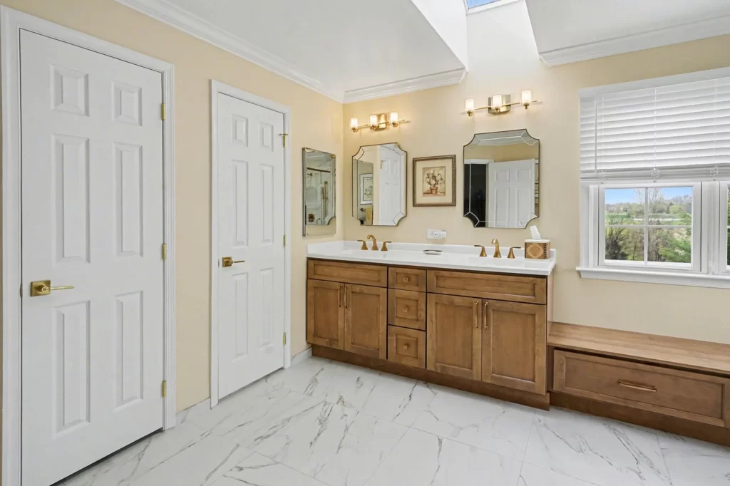 Master bathroom with double vanity, honey-wood cabinetry, ornate framed mirrors, large windows with scenic views, and marble flooring.