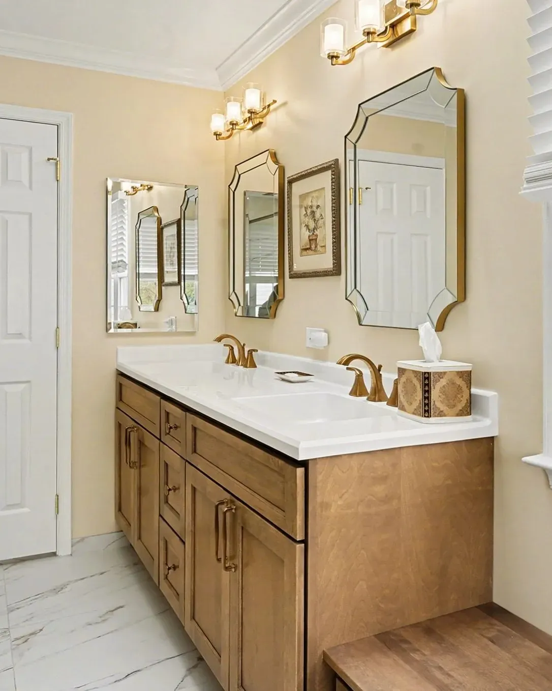 Elegant master bathroom with double vanity, ornate gold-framed mirrors, cream walls, and honey-wood cabinetry with white quartz countertop.