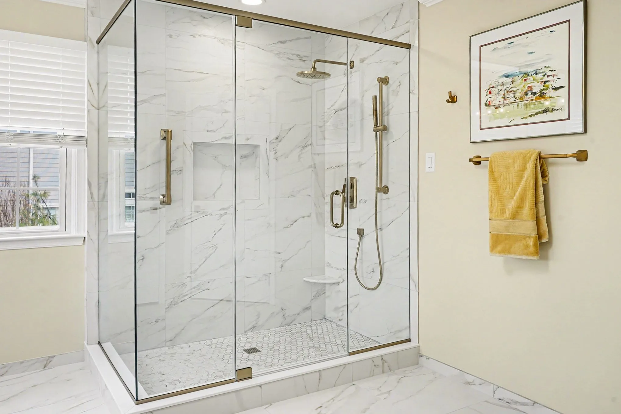 Homepage 29 Corner walk-in shower with marble subway tile walls, frameless glass doors, gold fixtures, and hexagonal marble mosaic floor.