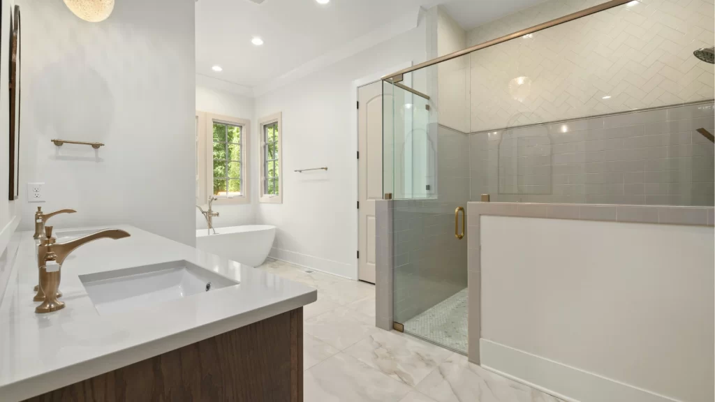 Modern bathroom remodel with white marble tile, frameless glass shower enclosure, and dual vanity with bronze fixtures