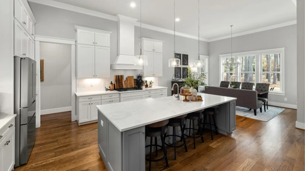 Open-concept kitchen with white upper cabinets, gray contrasting island, white quartz countertops, hardwood floors, and glass pendant lights