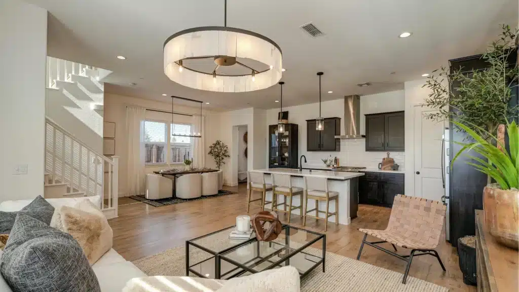 Modern open-concept home with white kitchen, black cabinets, island seating, hardwood floors, and contemporary pendant lighting