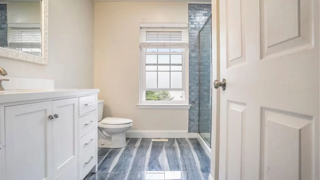 Modern bathroom remodel with white vanity, blue-gray tile shower, and wood-grain vinyl flooring