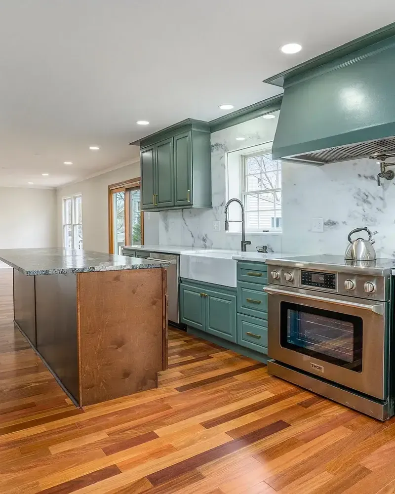Modern kitchen remodel with green shaker cabinets, marble backsplash, stainless steel appliances, and hardwood flooring by Pottstown Construction Company.