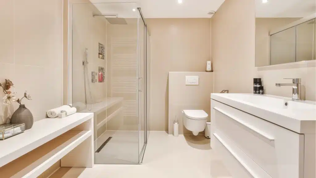 Modern luxury bathroom remodel with glass shower enclosure, white vanity, and beige tile walls
