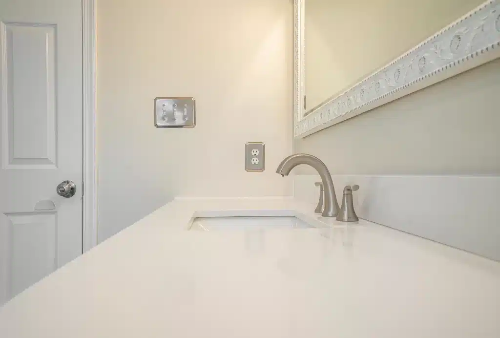 White bathroom vanity countertop with brushed nickel faucet and framed mirror
