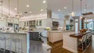 Large white kitchen with double islands, pendant lighting, dark wood bar top, and built-in appliances