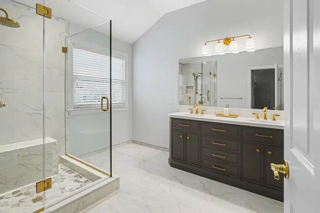 Modern bathroom with frameless glass shower, gray double vanity, and gold fixtures