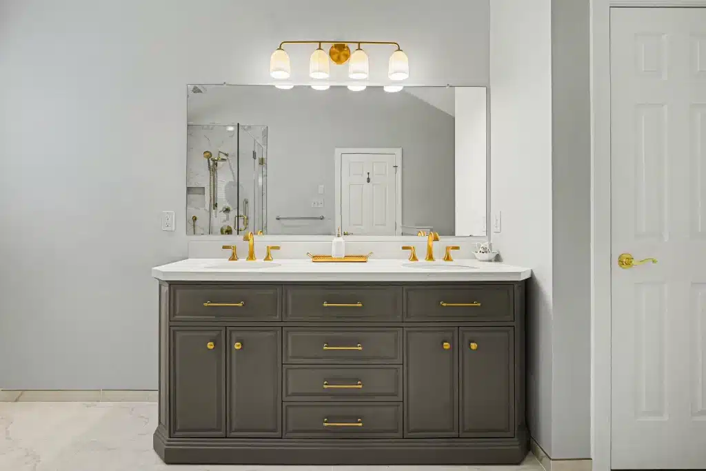 Gray bathroom vanity with dual sinks, gold hardware, and large wall mirror