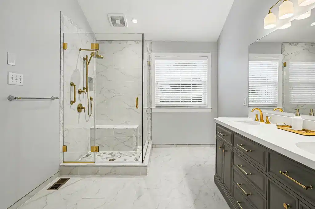 Bathroom remodel with gray double vanity, glass shower, and marble-look tile floor