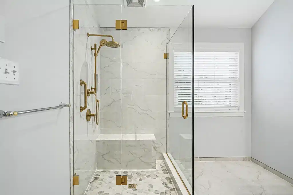 Walk-in shower with marble-look tile, brass fixtures, and frameless glass panels