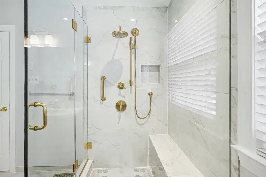 Glass shower with marble-look tile walls, built-in bench, and brass fixtures
