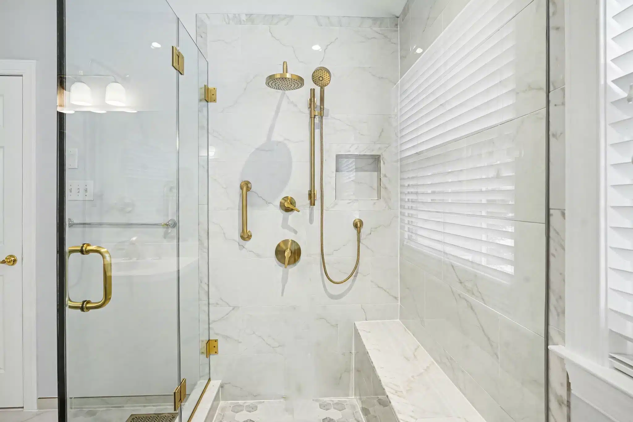 Glass shower with marble-look tile walls, built-in bench, and brass fixtures