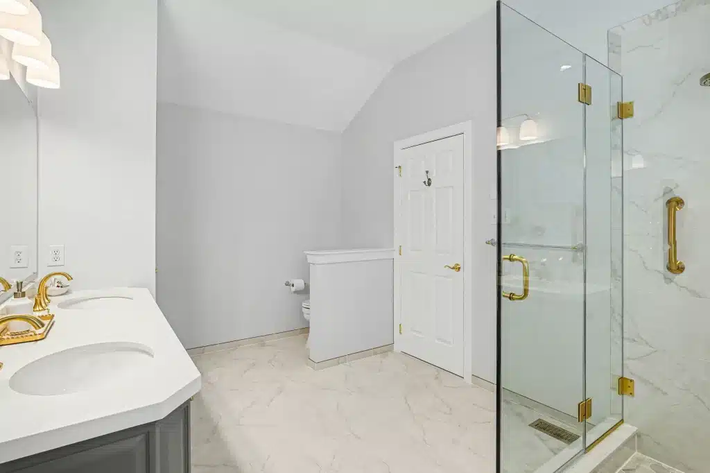 Bathroom corner with glass shower, gray vanity, toilet, and light tile flooring