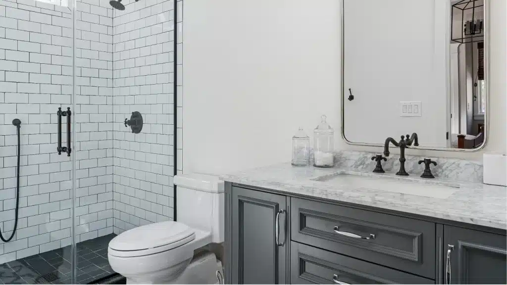Modern bathroom remodel with white subway tile shower, marble countertop, gray vanity, and black fixtures by Pottstown Construction Company