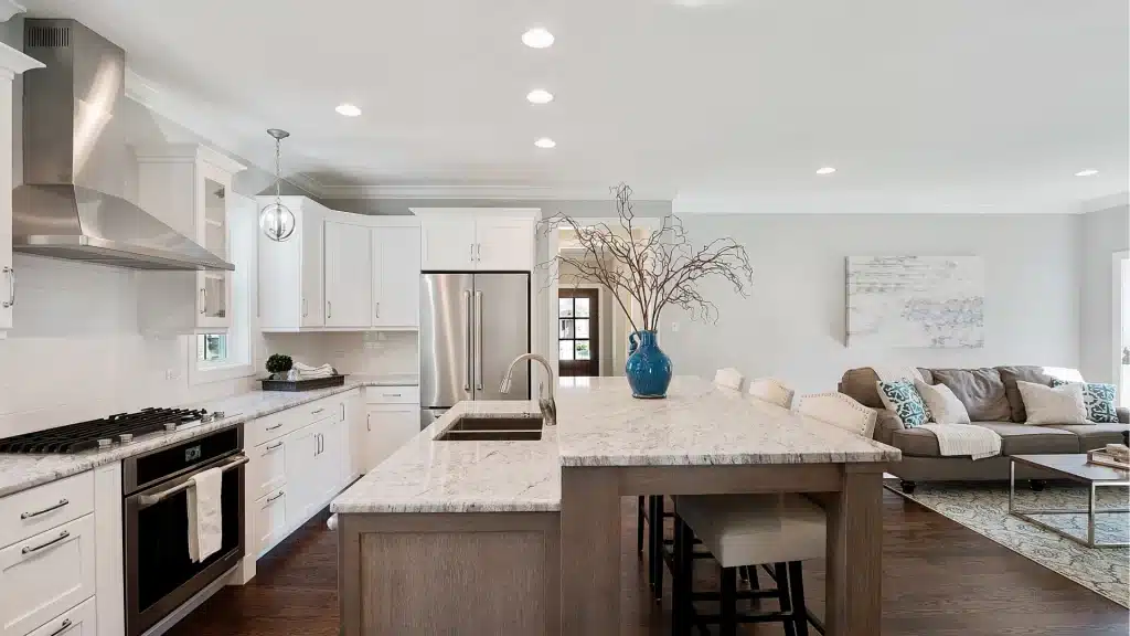 Open-concept kitchen with oversized marble island, white cabinetry, and adjoining living room seating