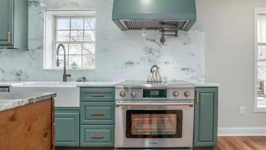 Teal kitchen remodel featuring a marble backsplash, wall-mounted pot filler above a Thor stainless steel range, and a farmhouse sink