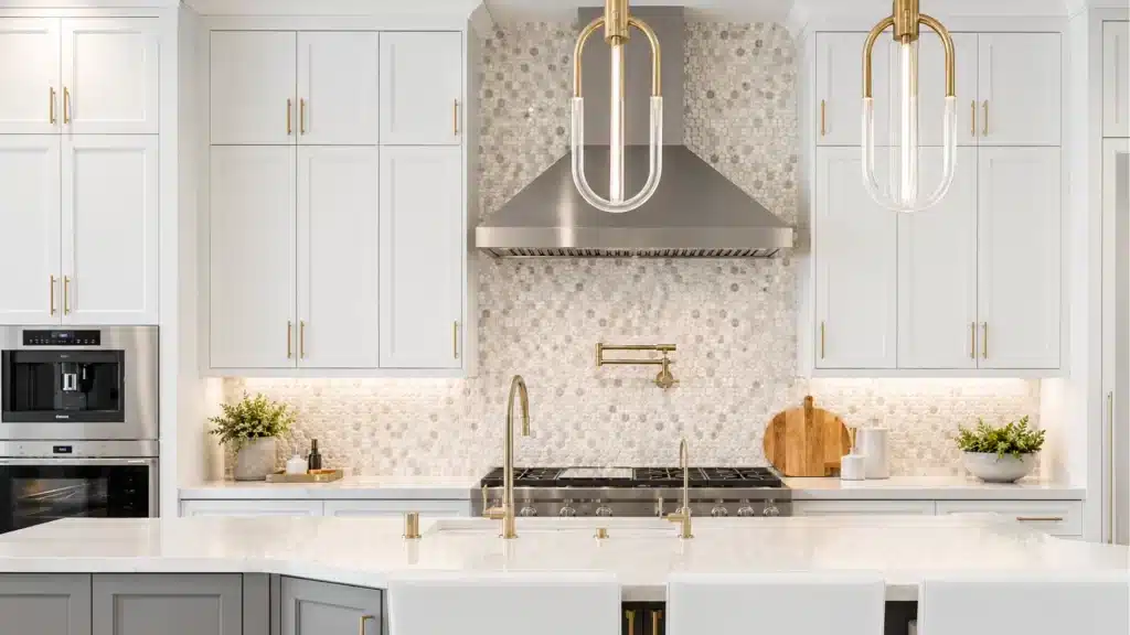 Luxury white kitchen with hexagonal mosaic tile backsplash, brass pot filler above a gas cooktop, gold pendant lights, and an island with a bridge faucet