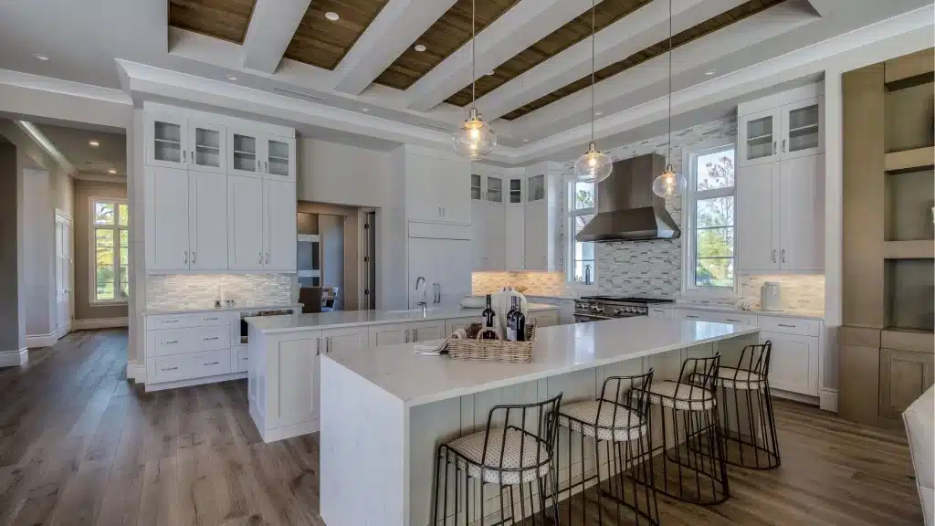 White kitchen remodel with oversized island, glass pendant lights, and coffered wood ceiling beams